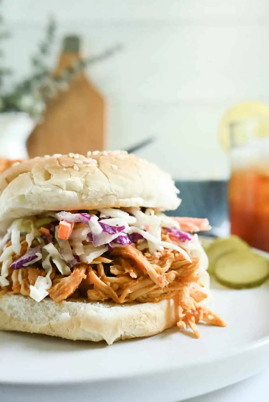 Bun piled high with crockpot pulled chicken and coleslaw and set on a white plate.