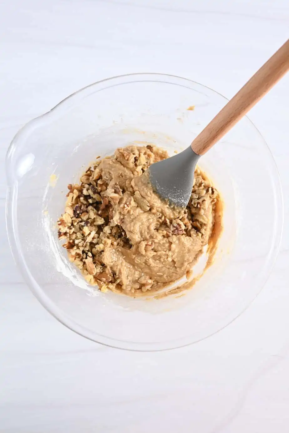 Walnuts being folded into maple walnut blondie batter in a glass bowl.