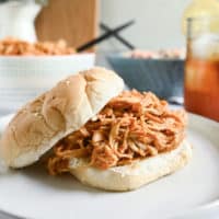 Crockpot pulled chicken on a bun, set on a white plate.