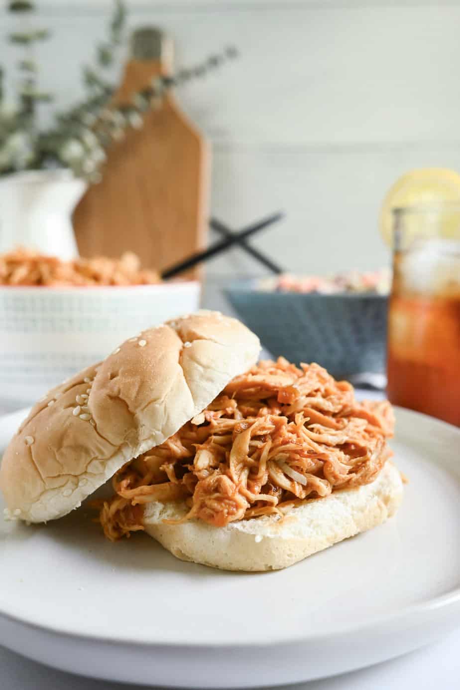 Sesame bun topped with crockpot pulled chicken, set on a white plate.