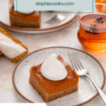 Plated slice of pumpkin spice cake topped with a dollop of whipped cream, with a plate of 2 slices in the background. Text overlay includes recipe name.