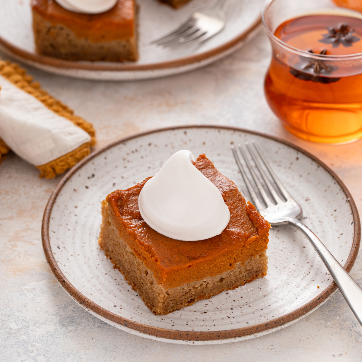 Slice of pumpkin spice cake topped with a dollop of whipped cream on a plate.