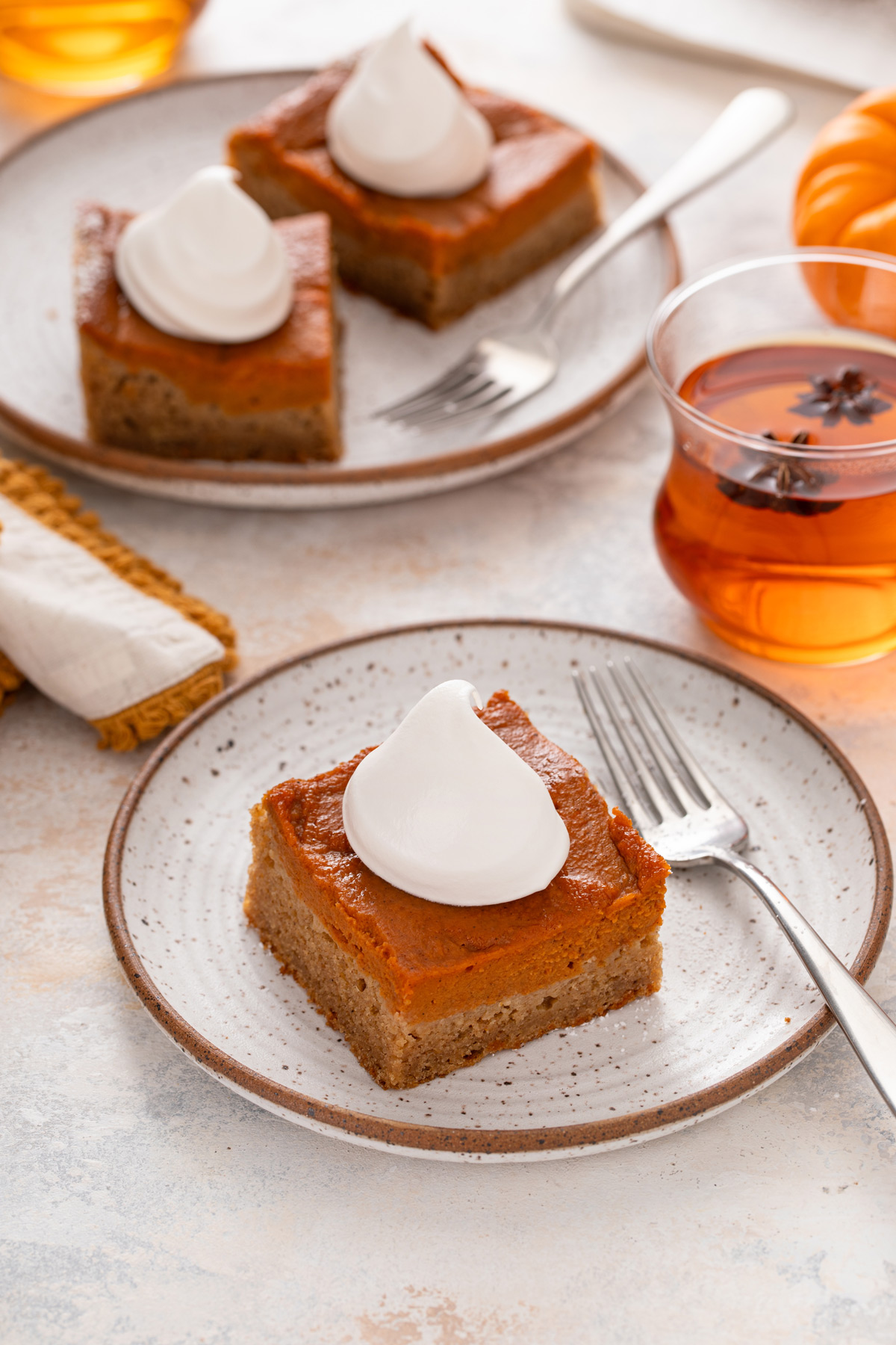 Plated slice of pumpkin spice cake topped with a dollop of whipped cream, with a plate of 2 slices in the background.