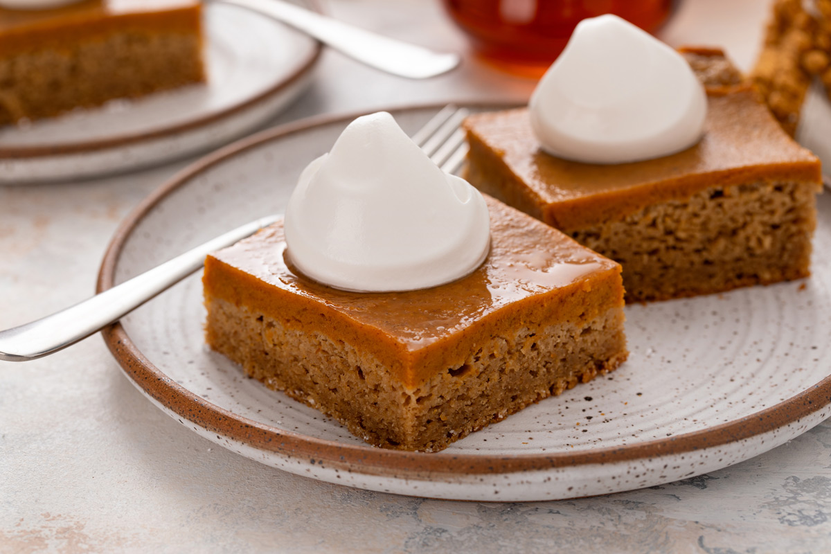 Two slices of pumpkin spice cake on a plate, each topped with a dollop of whipped cream.