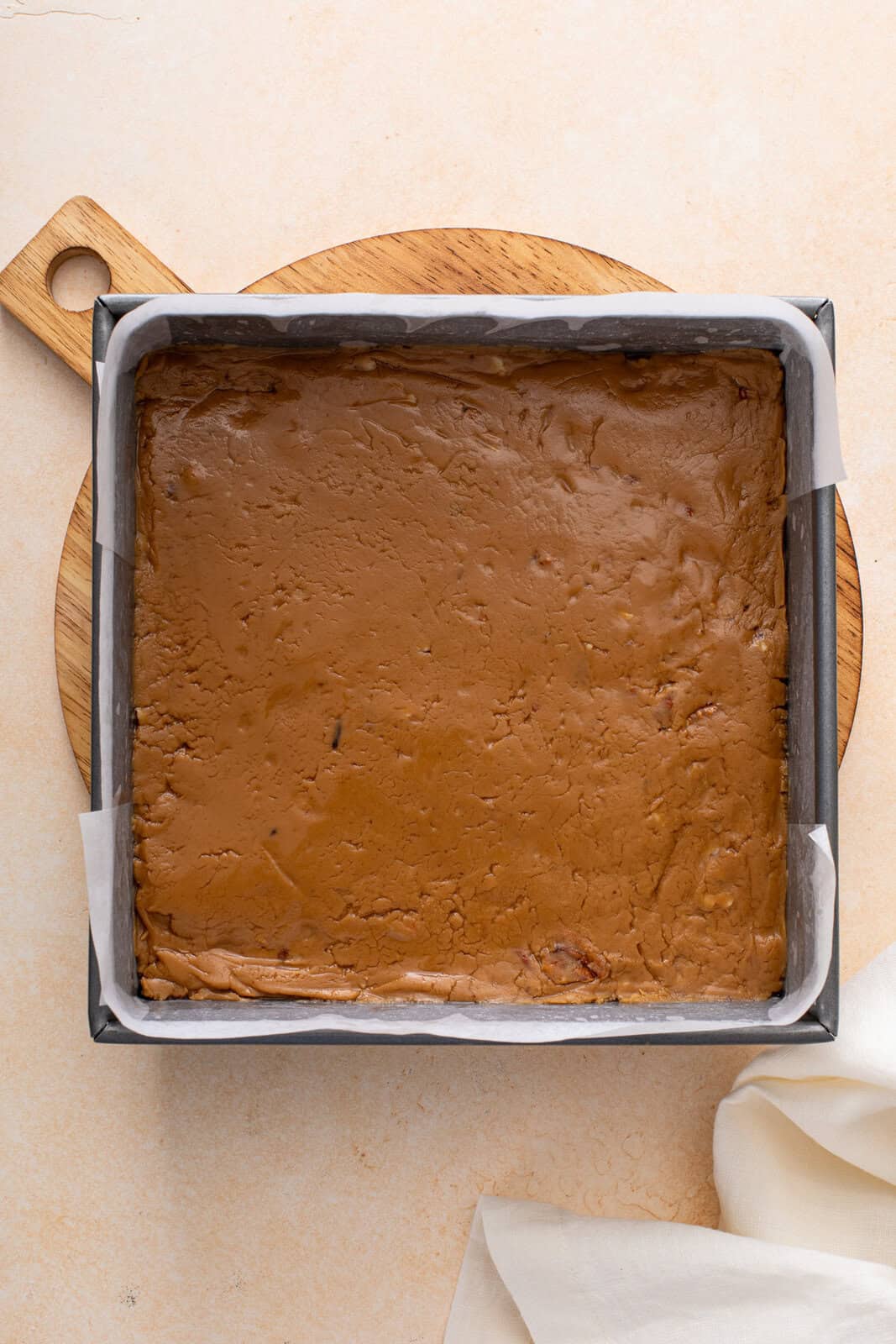 Brown sugar fudge spread into a lined cake pan, ready to cool.