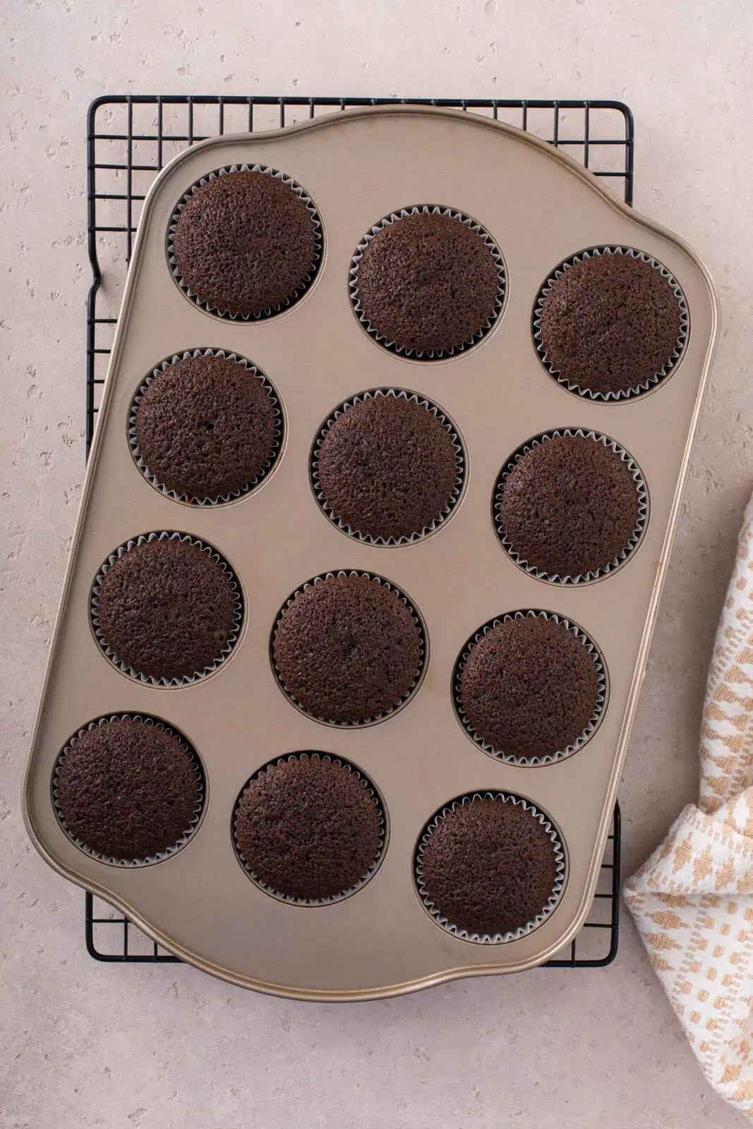 A pan of baked chocolate cupcakes in a cupcake pan, set on a wire rack.