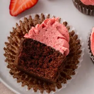 Bite taken from a chocolate cupcake topped with strawberry frosting.
