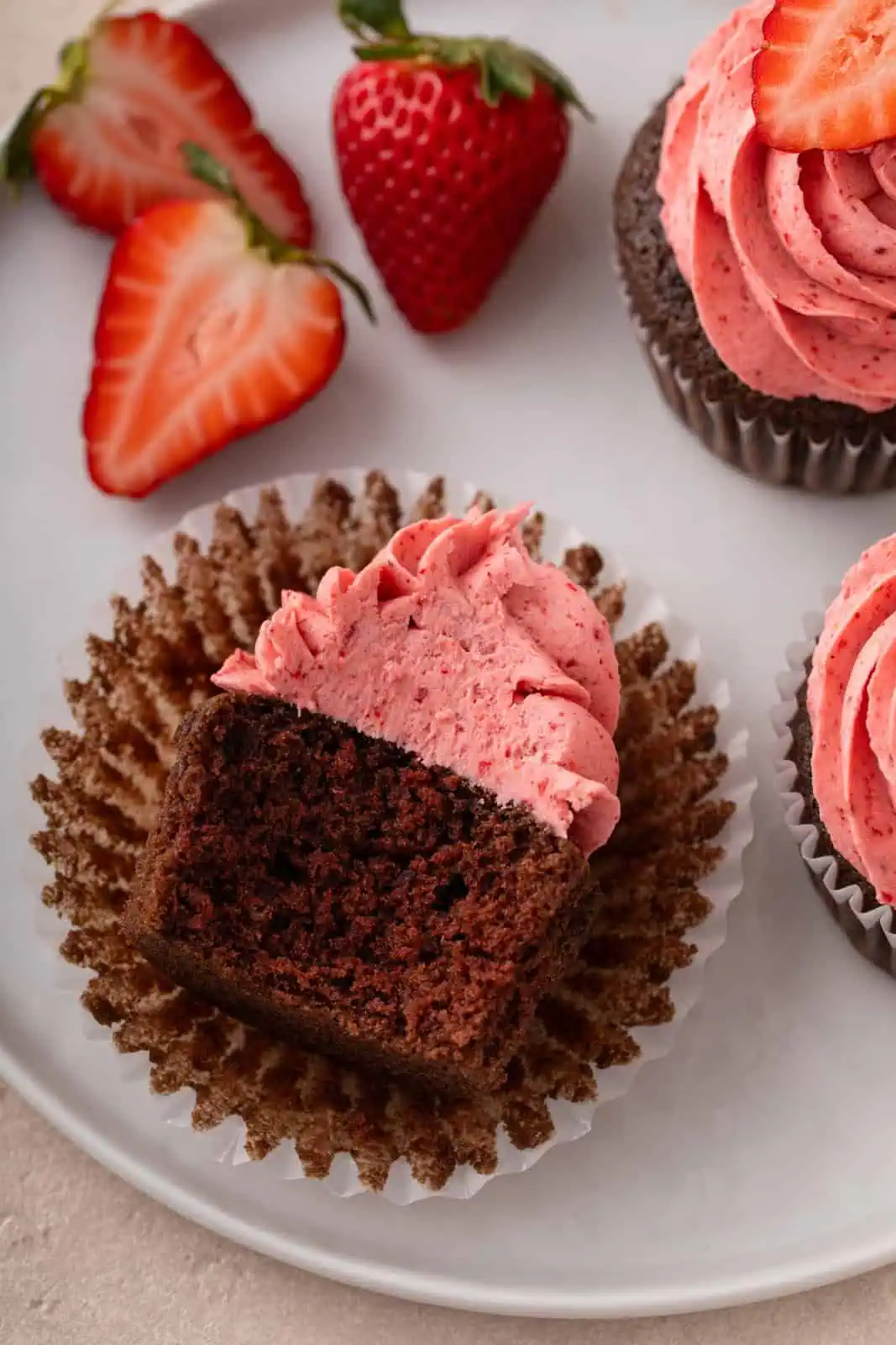 Bite taken from an easy chocolate cupcake topped with strawberry frosting, laying on its side on a white plate.