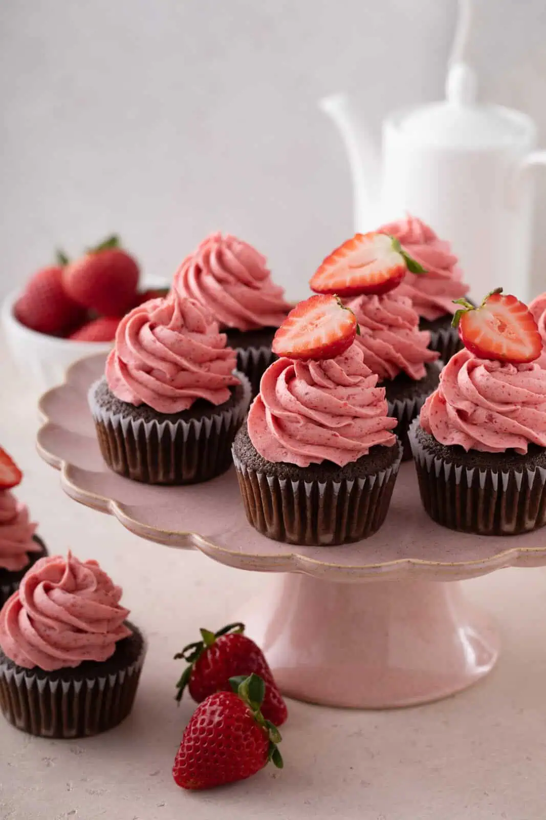 Chocolate cupcakes topped with strawberry frosting arranged on a pink cake stand.