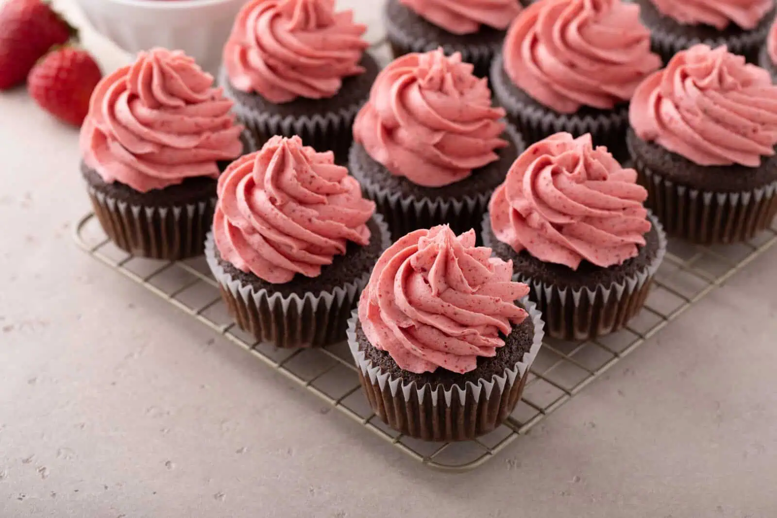 Chocolate cupcakes topped with strawberry frosting arranged on a wire rack.