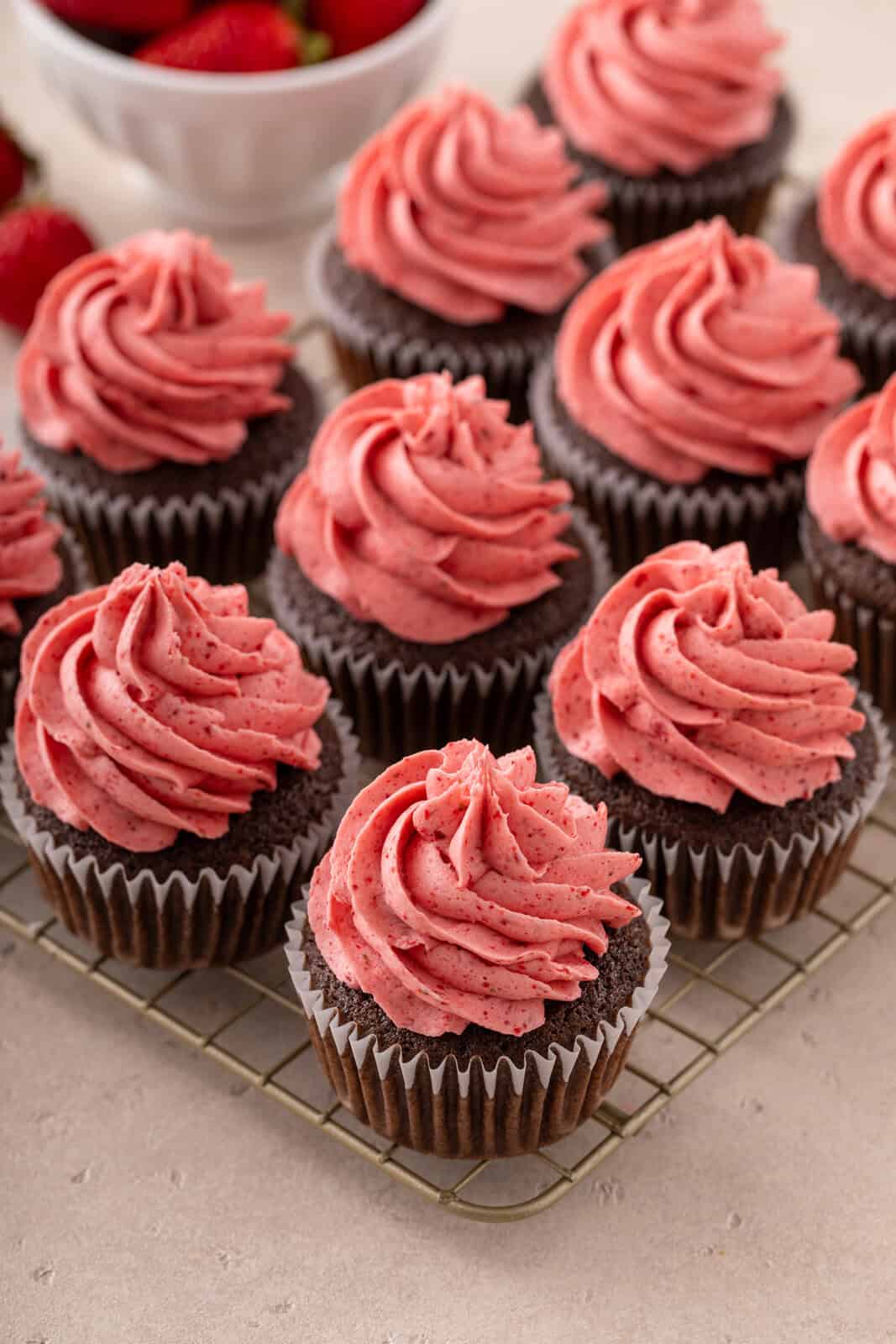 Strawberry buttercream piped onto chocolate cupcakes on a wire rack.