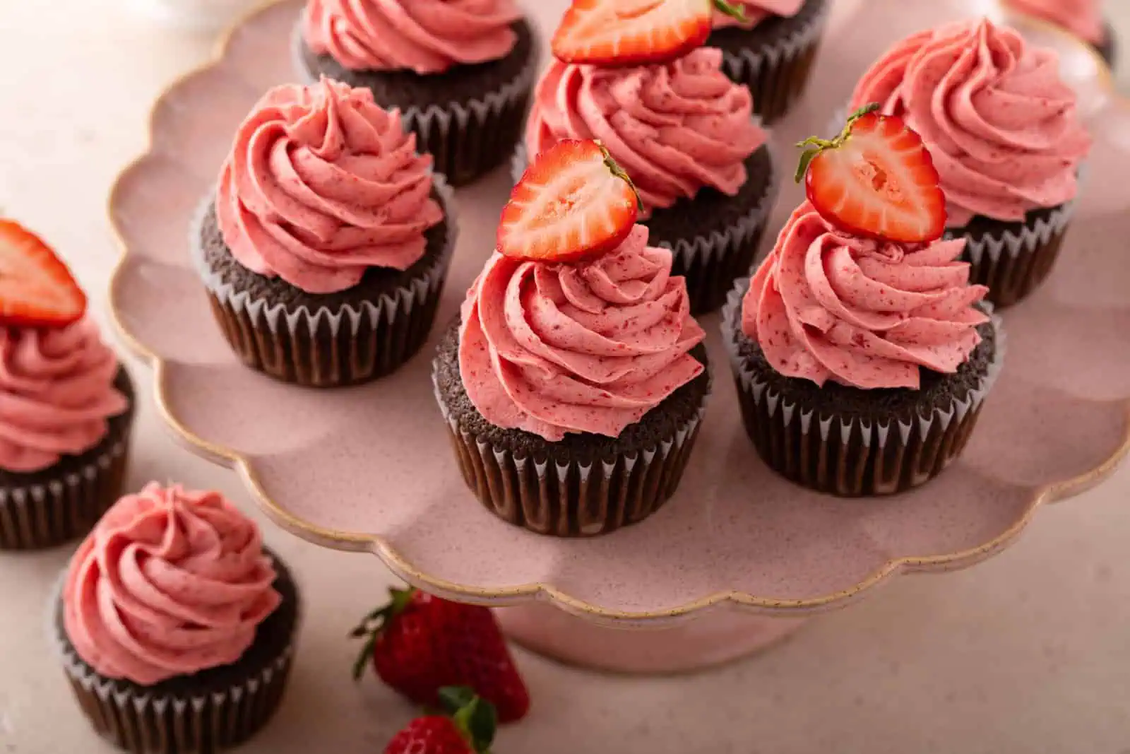 Several strawberry-frosted easy chocolate cupcakes arranged on a pink cake stand.