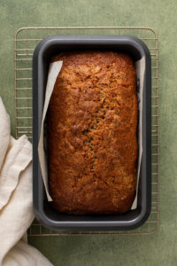 Cooling loaf of bisquick banana bread in a parchment-lined loaf pan on a wire rack.