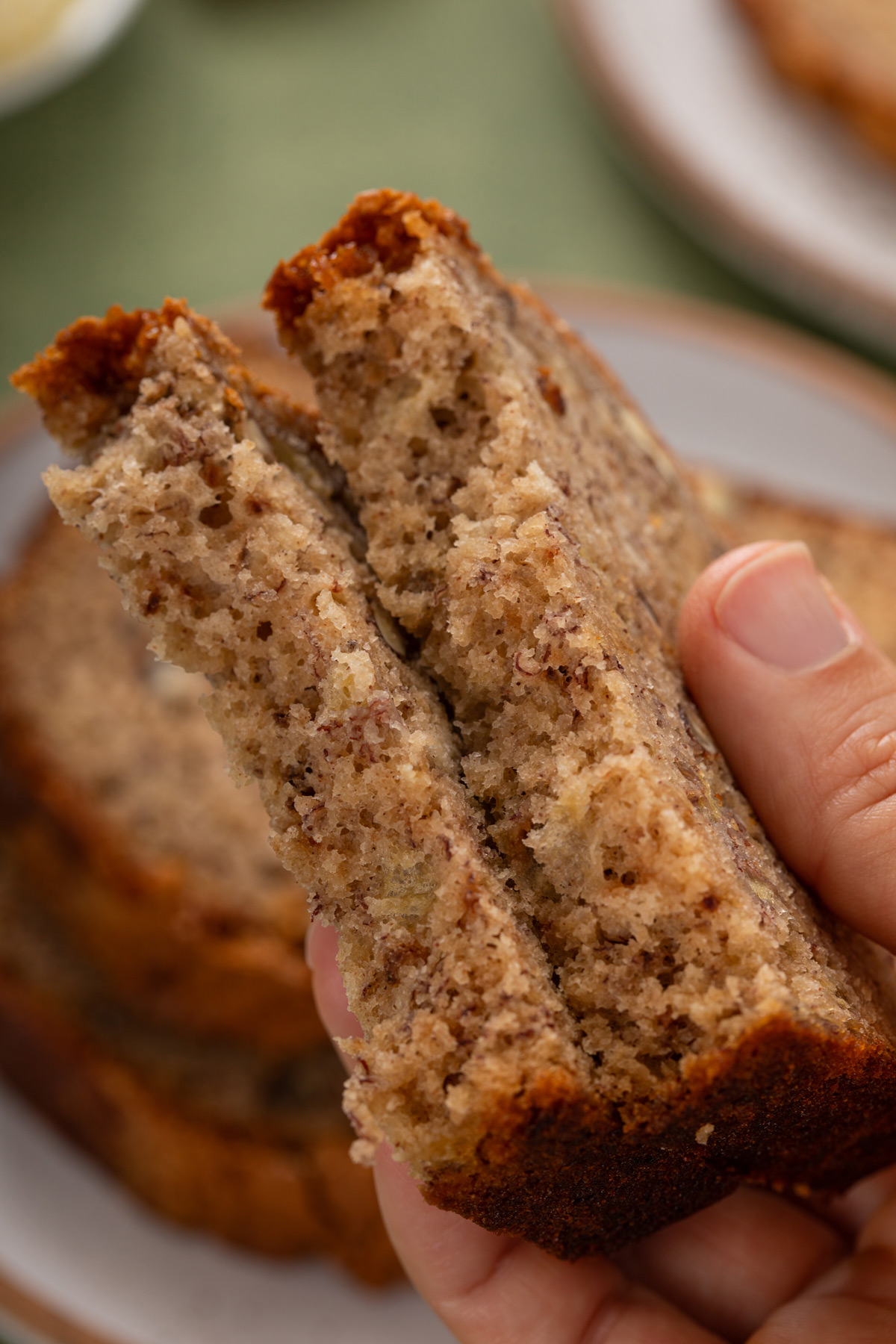 Person holding up a slice of bisquick banana bread that's been broken in half to show the moist crumb.