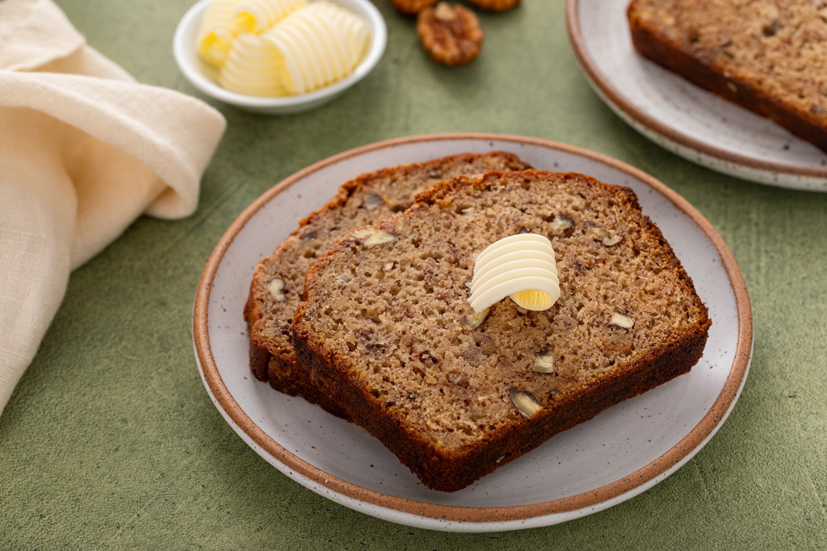 Two slices of bisquick banana bread on a plate with a pat of butter on top.