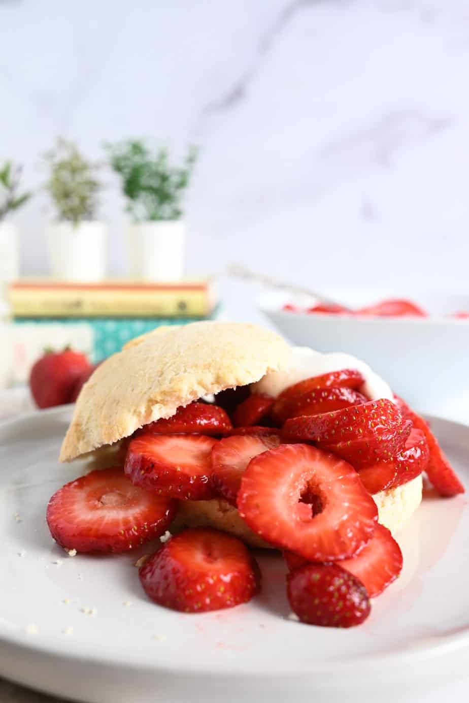 White plate with strawberry shortcake topped with whipped cream and sliced strawberries.