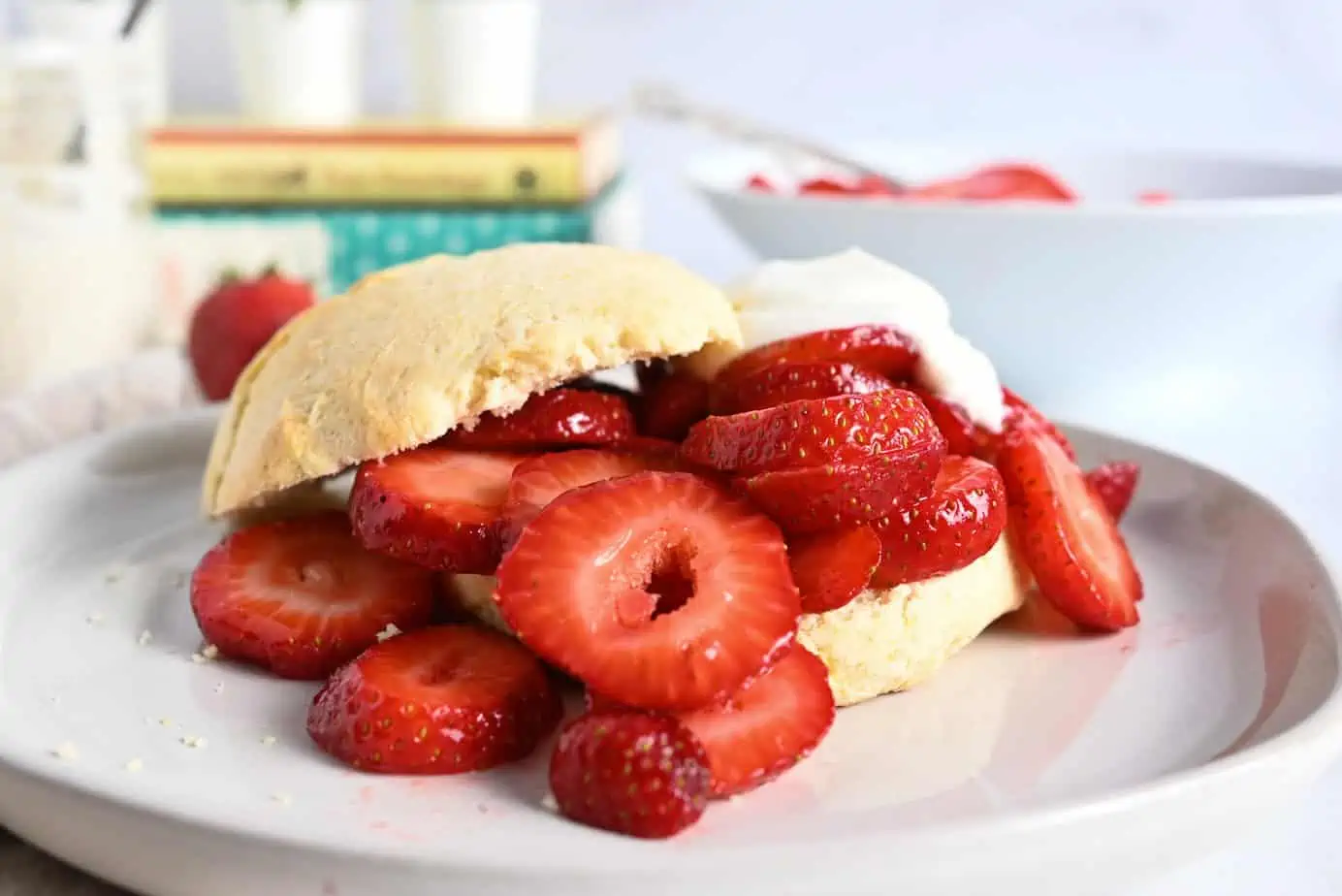 Shortcake biscuit on a white plate, topped with sliced strawberries and whipped cream.