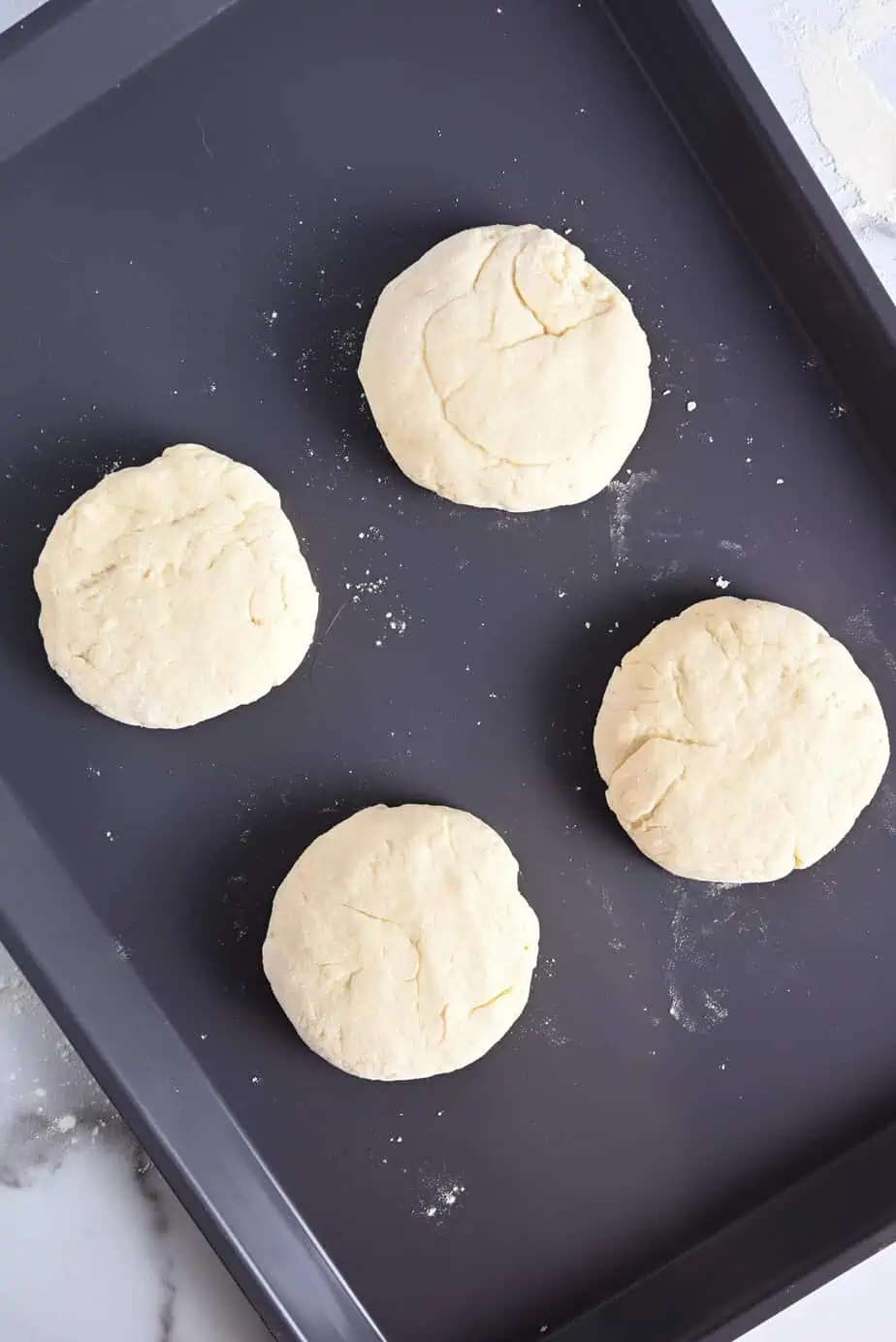 Four unbaked shortcakes on a baking sheet, ready to go in the oven.