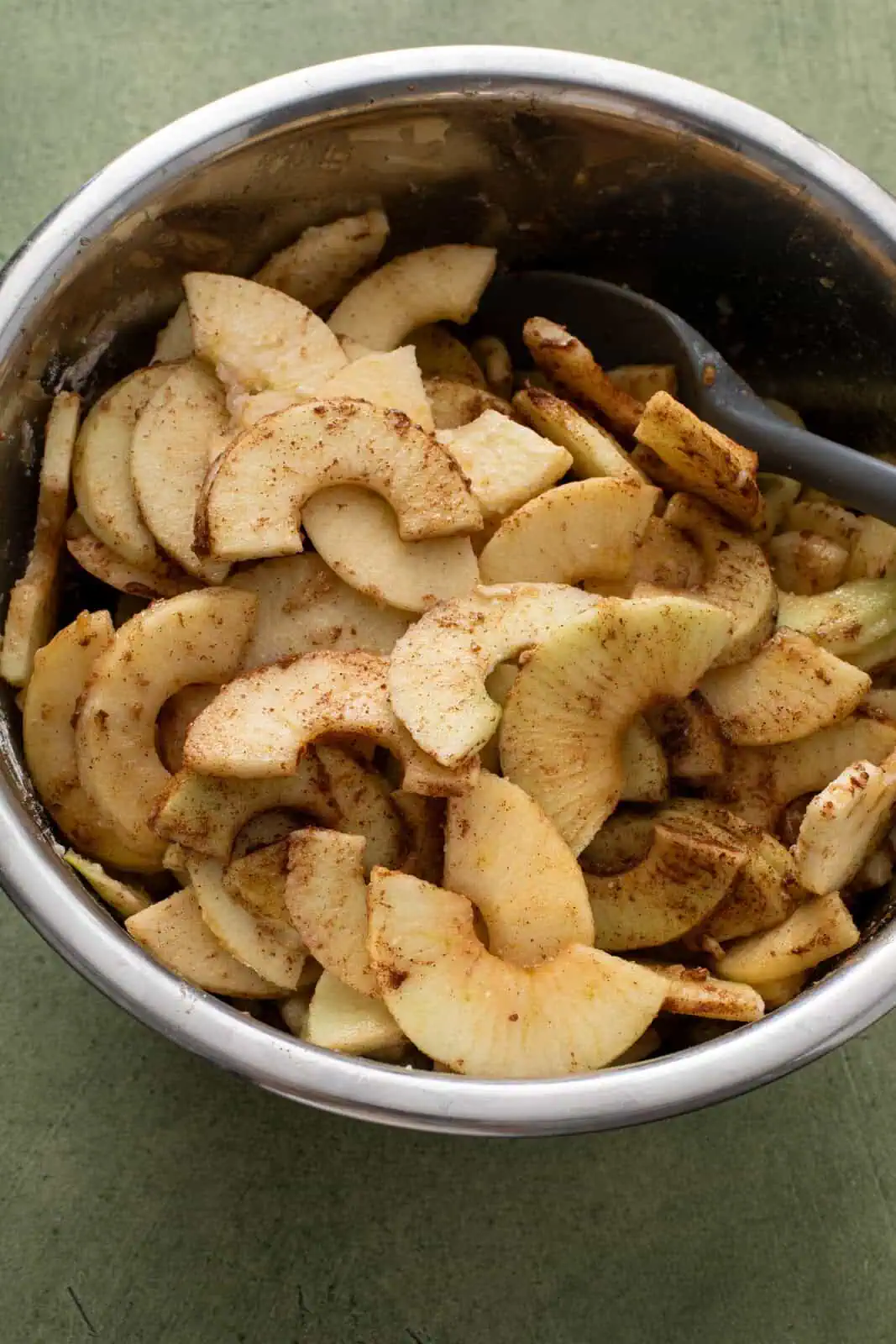 Filling for dutch apple pie stirred together in a large metal mixing bowl.