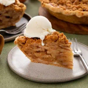 Plated slice of dutch apple pie topped with a scoop of vanilla ice cream.