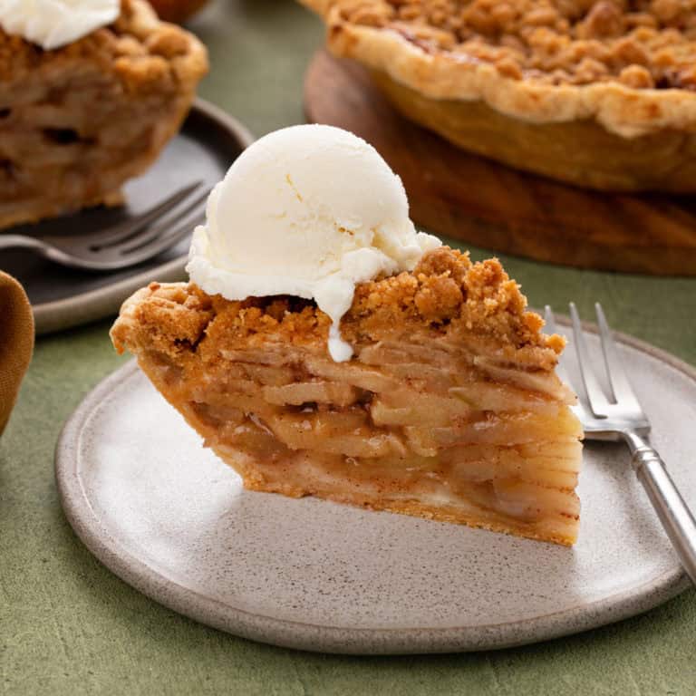 Plated slice of dutch apple pie topped with a scoop of vanilla ice cream.
