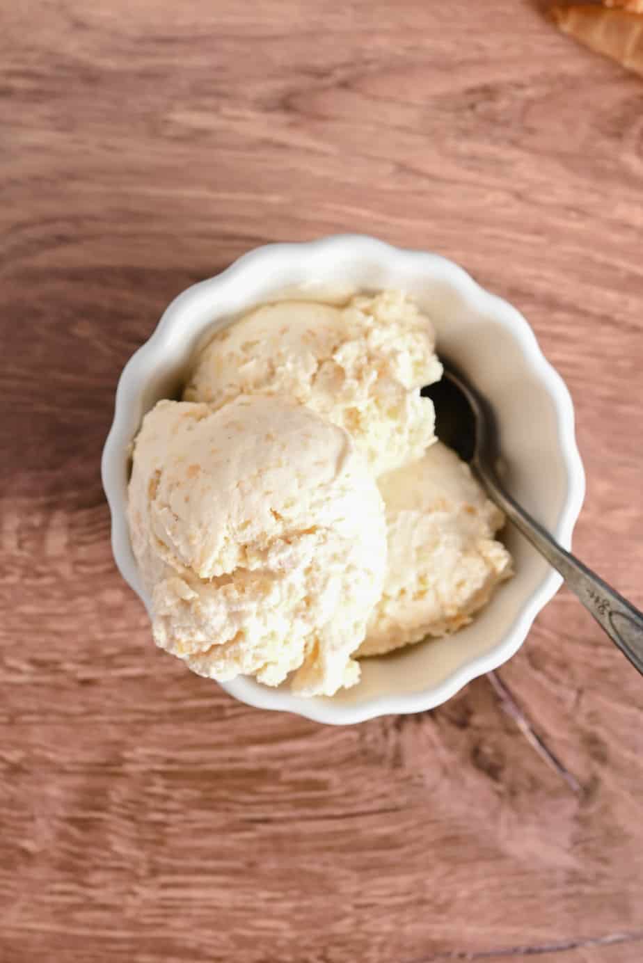 Close up of peach ice cream in a white bowl with a spoon in it.