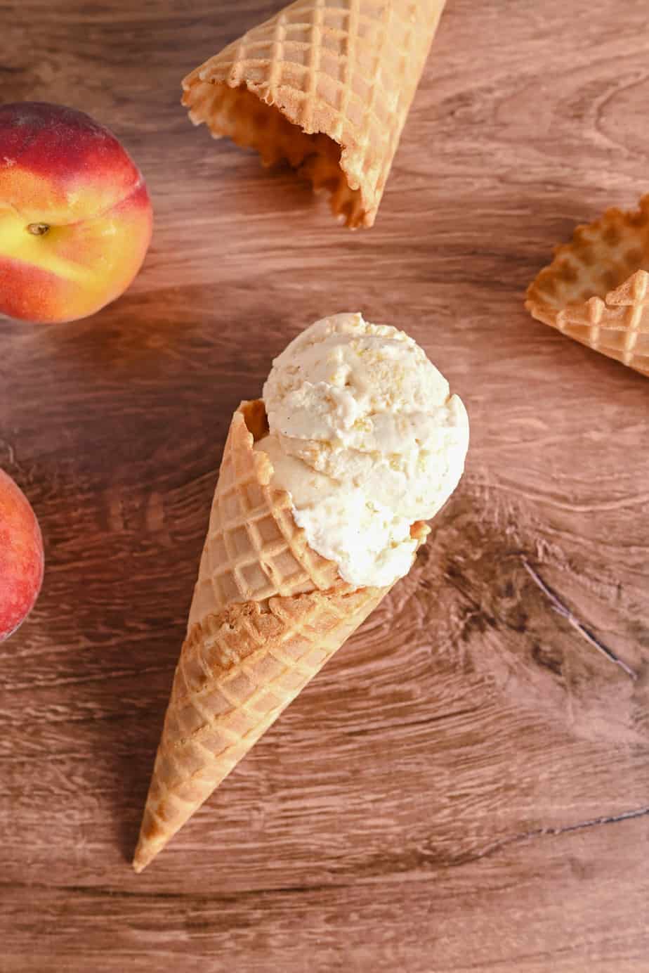Peach ice cream in a waffle cone on a wooden countertop amongst empty waffle cones.