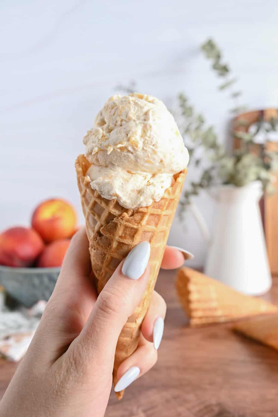 Hand holding a waffle cone with a scoop of peach ice cream in it.