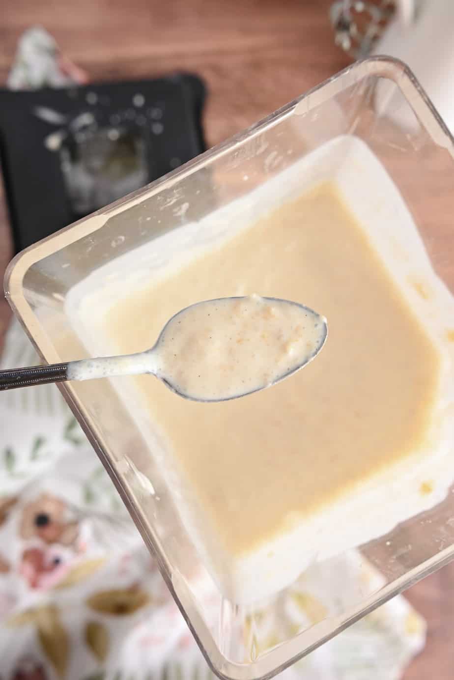 Spoon holding a spoonful of peach ice cream base over a blender pitcher filled with the ice cream base.