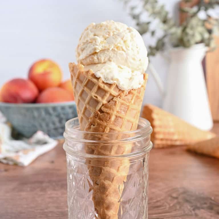 Peach ice cream in a waffle cone being held upright in a glass jar.