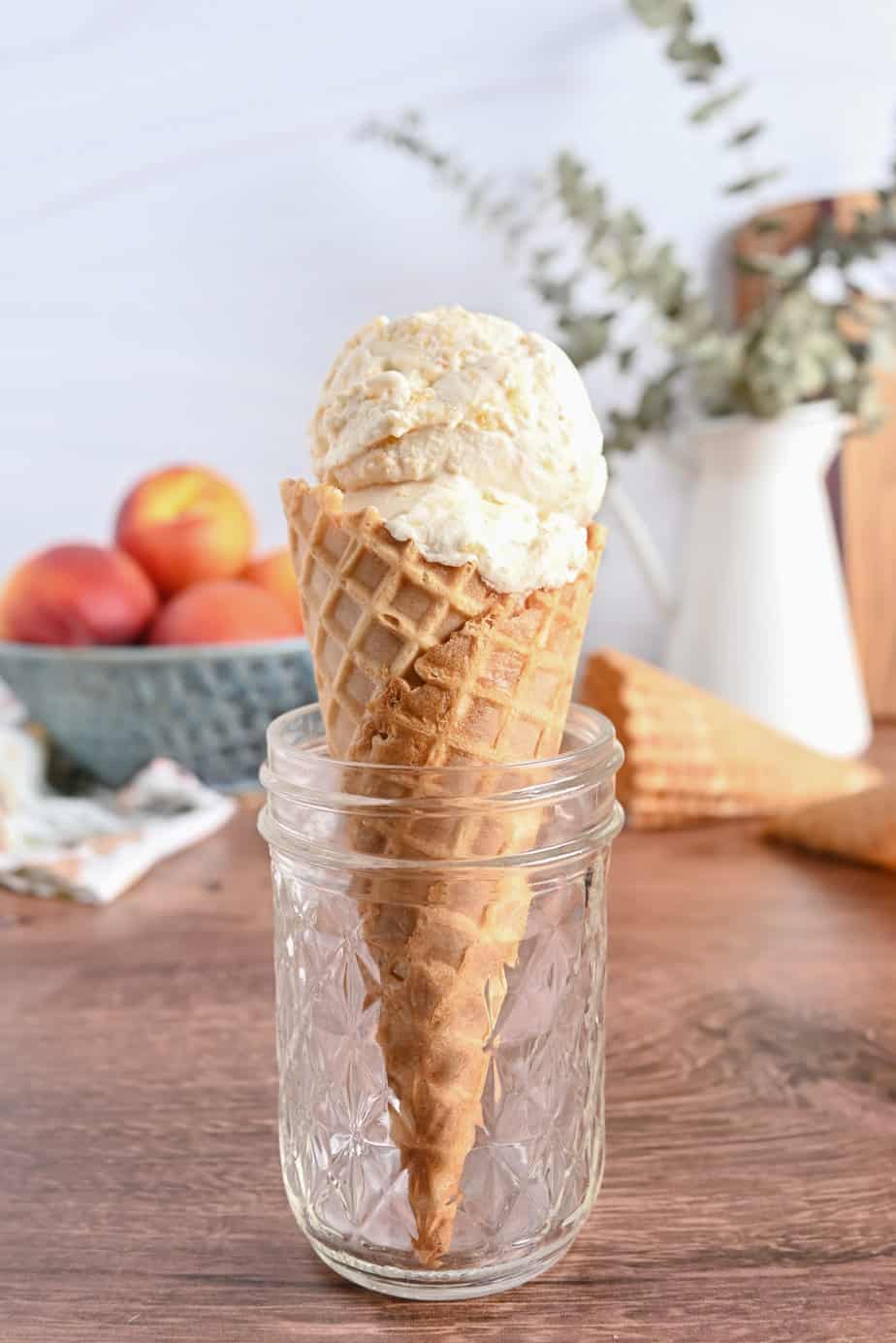 Glass jar holding up a waffle cone filled with peach ice cream.