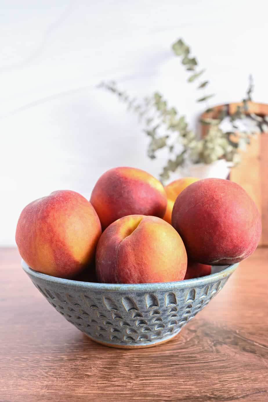 Blue pottery bowl filled with peaches set on a wooden countertop.