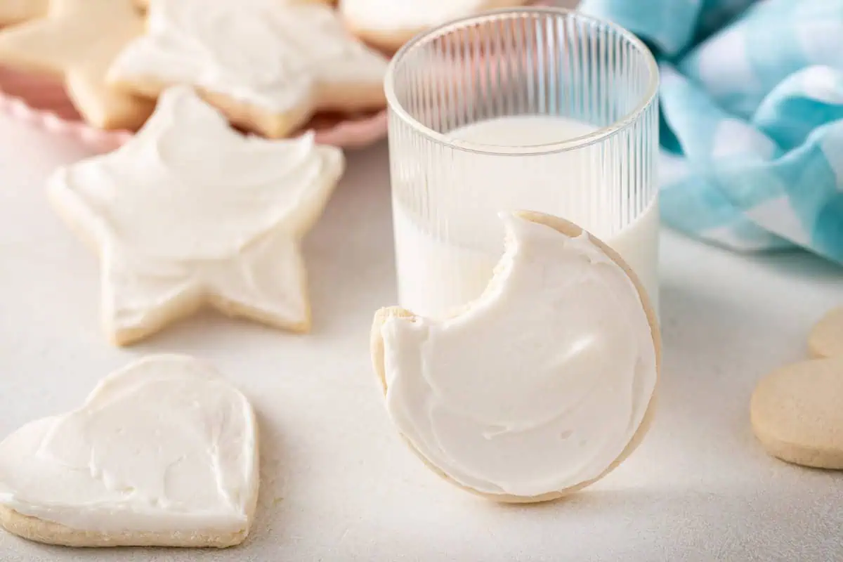 Round no chill sugar cookie with a bite taken from it, leaning against a glass of milk.