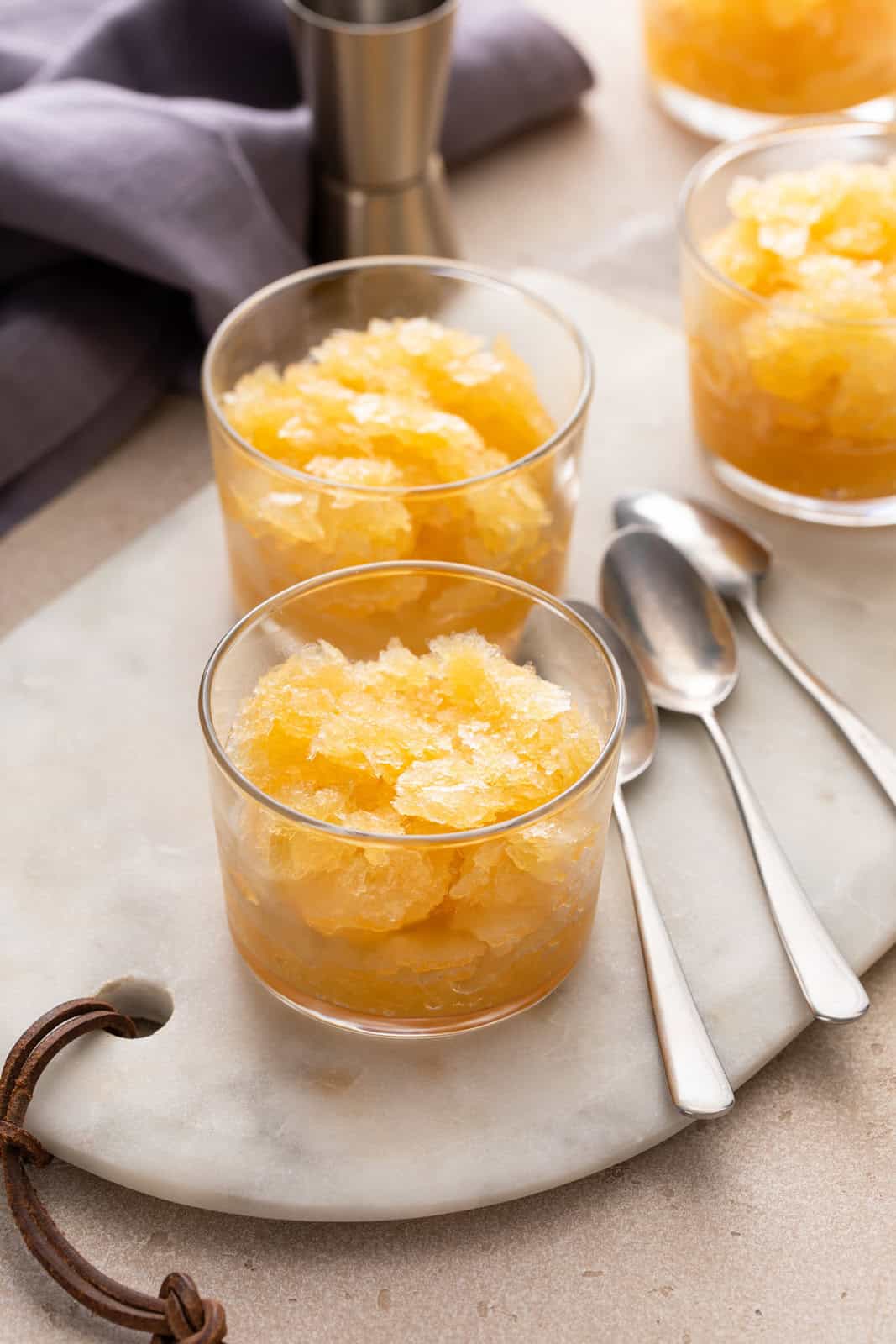 Three glasses of bourbon slush next to spoons on a marble board.