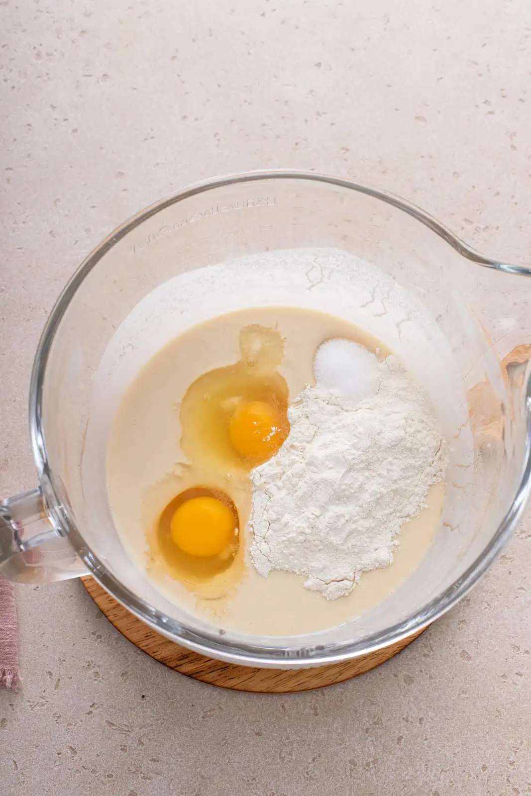 Eggs and more flour being added to roll dough base in a mixing bowl.