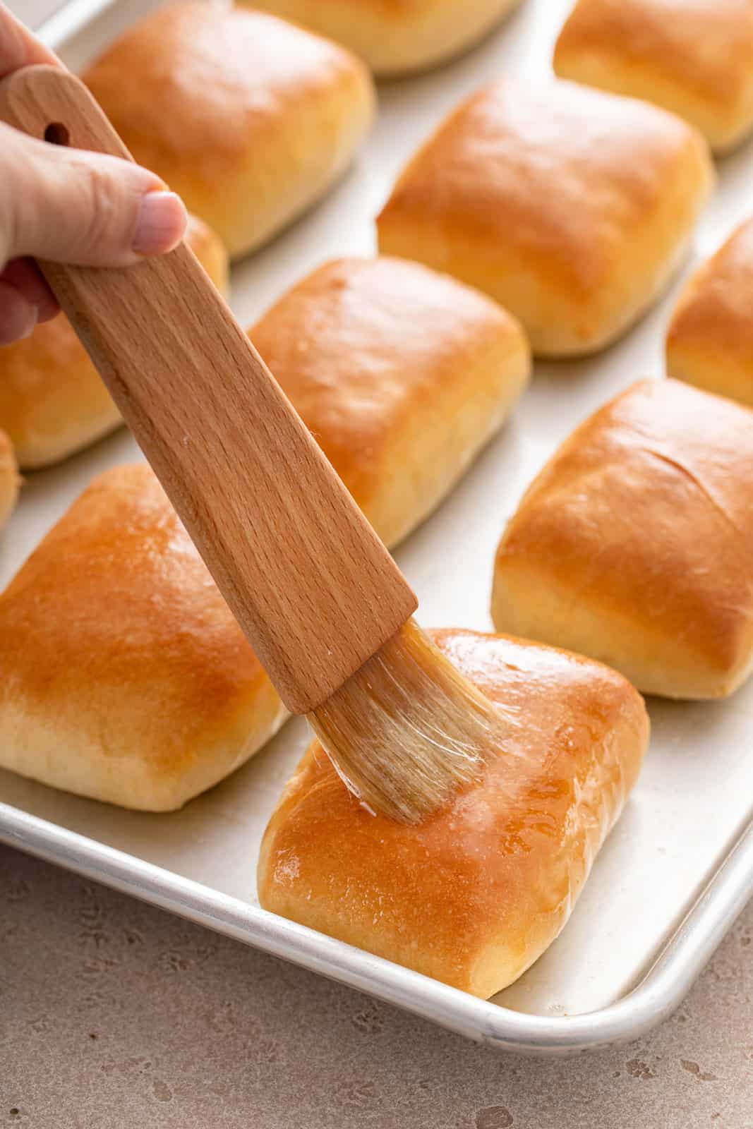 Brushing butter over texas roadhouse rolls on a baking sheet.