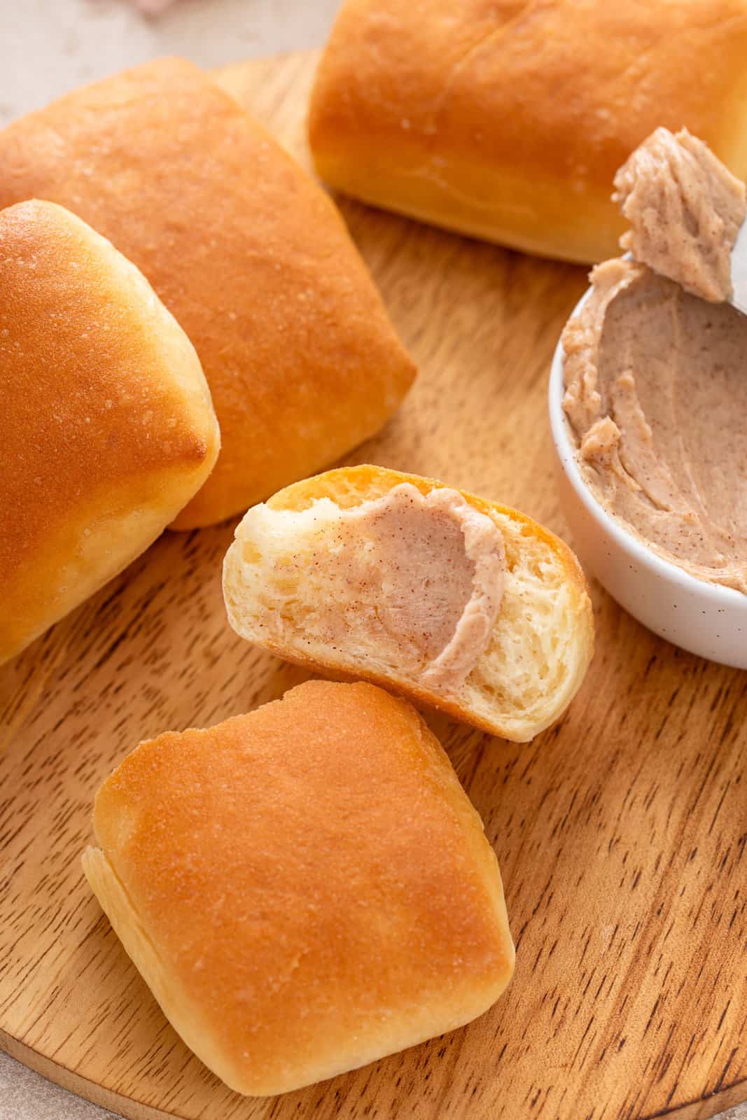 Cinnamon honey butter smeared onto a halved texas roadhouse roll on a wooden cutting board.