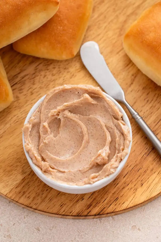 Overhead view of cinnamon honey butter in a white bowl, set next to a butter knife.