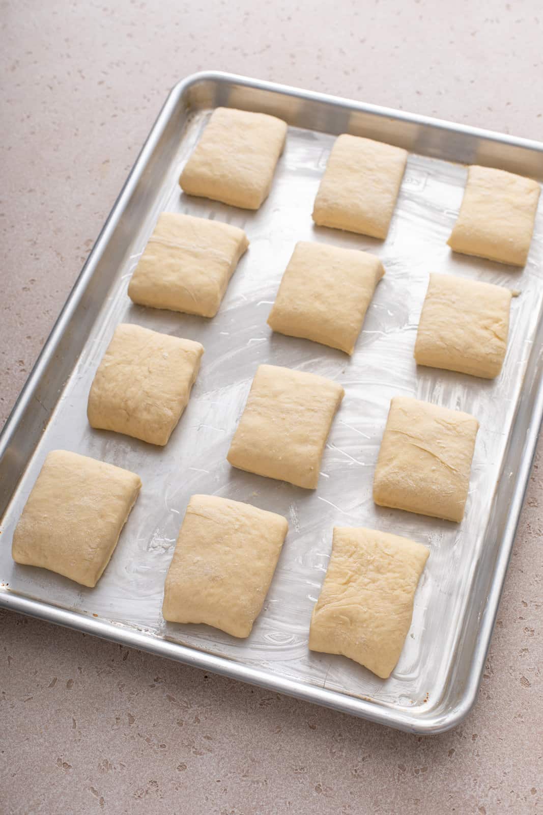 Cut texas roadhouse roll dough arranged on a buttered baking sheet.