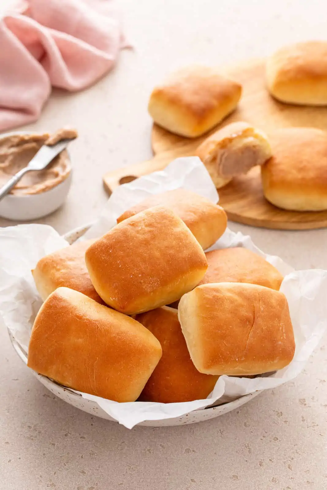 Texas Roadhouse rolls in a parchment-lined bowl with a board of more rolls visible in the background.