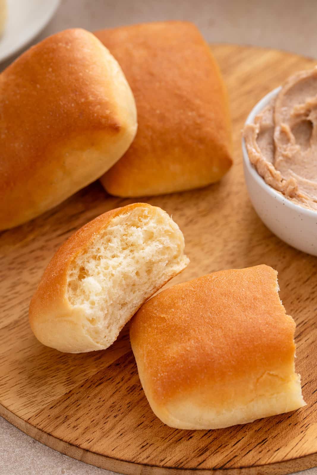 Texas roadhouse rolls arranged on a wooden board by a bowl of cinnamon honey butter. One of the rolls is torn in half.