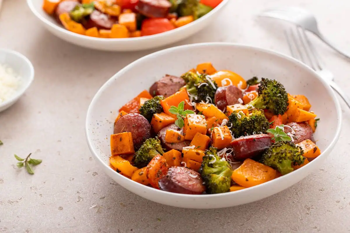 White bowl with sheet pan sausage and veggies on a countertop.