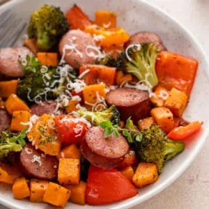 Sheet pan sausage and veggies in a white bowl.