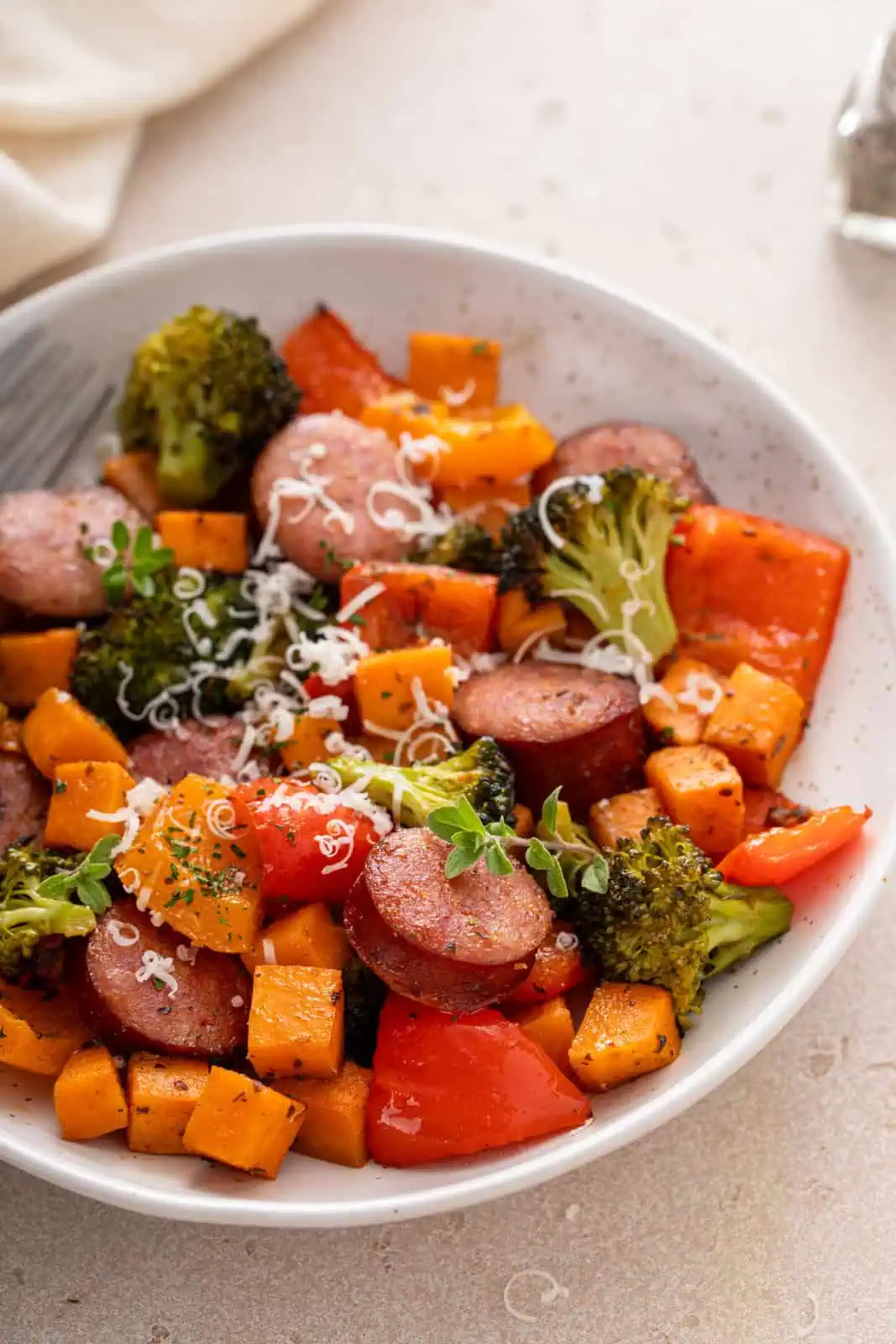 White bowl filled with sheet pan sausage and vegetables, garnished with parmesan cheese.