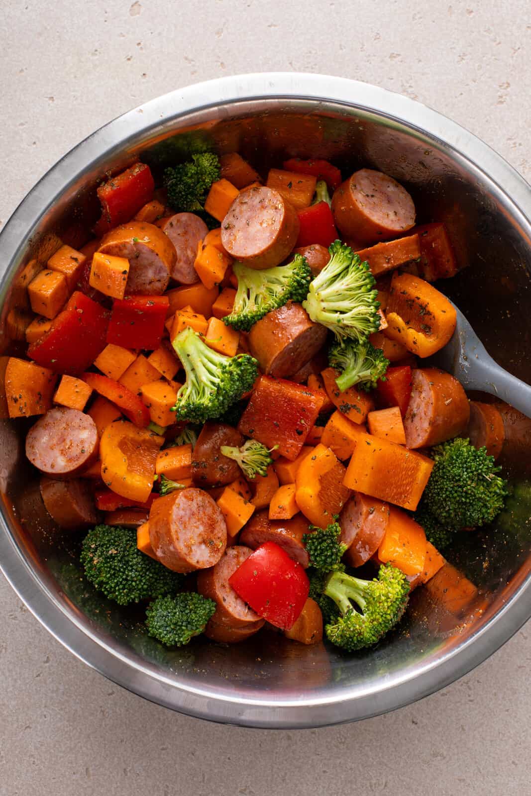 Smoked sausage and diced vegetables being mixed together in a metal bowl.