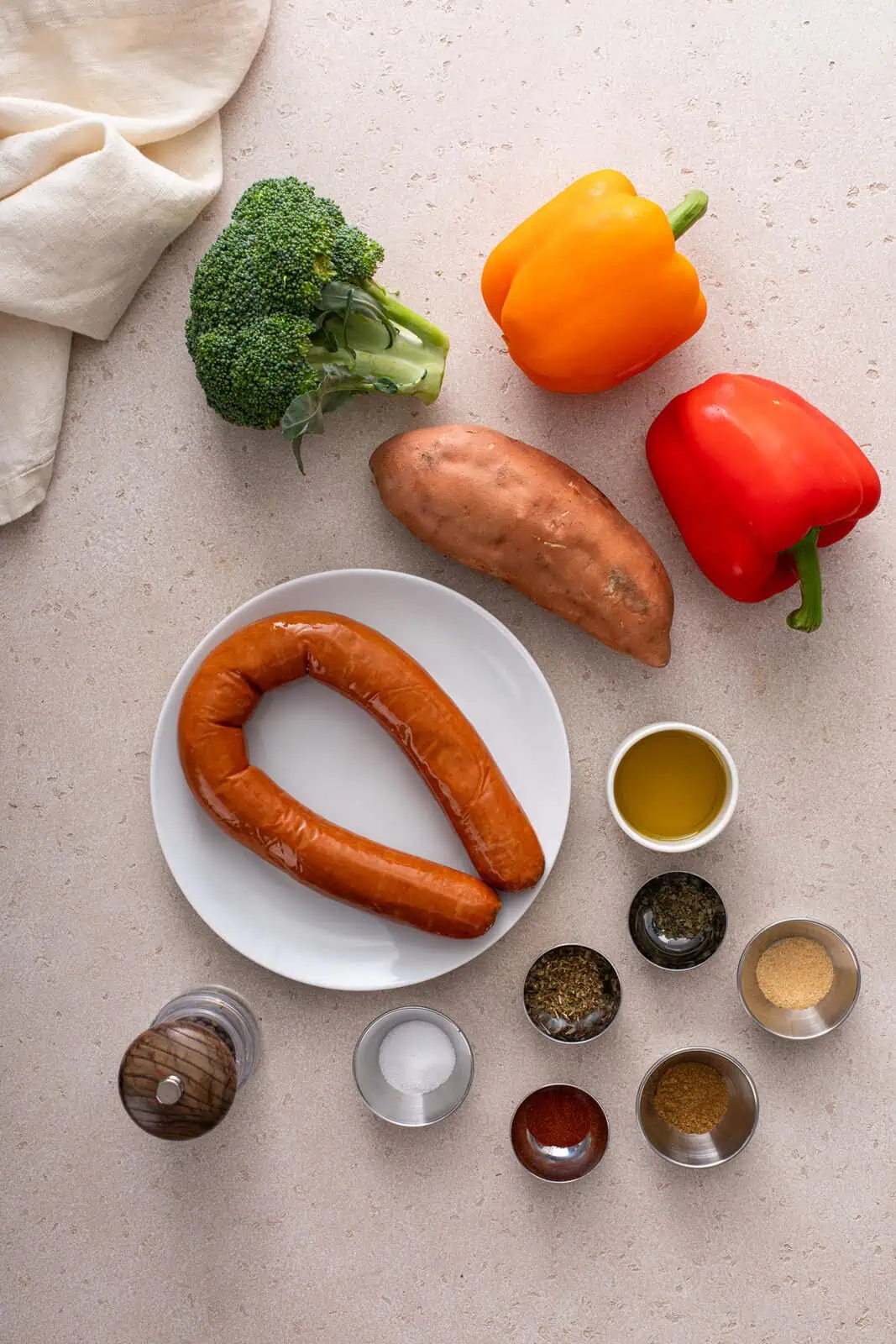 Ingredients for sheet pan sausage and veggies arranged on a beige countertop.