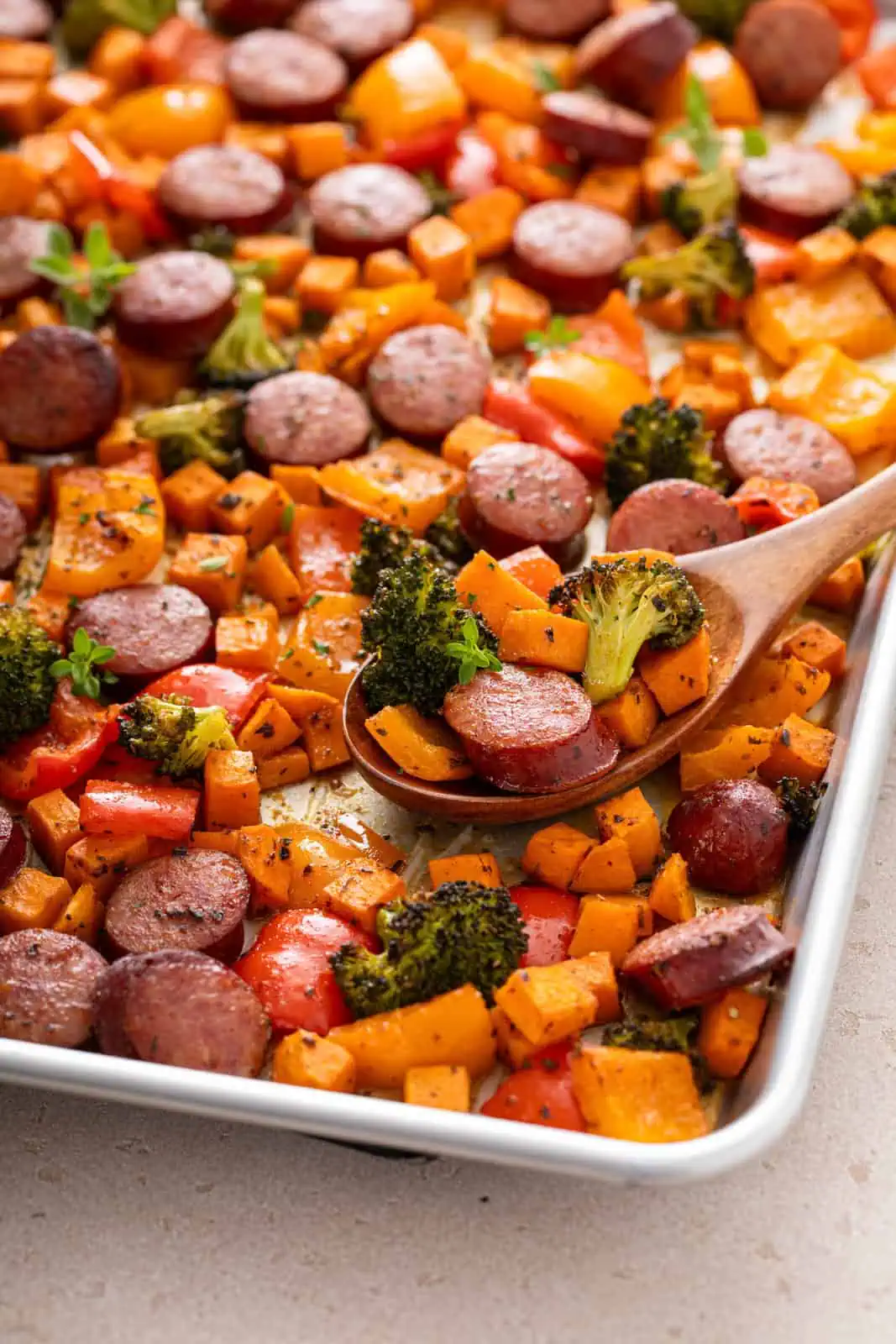 Wooden spoon filled with sausage and veggies on a sheet pan.