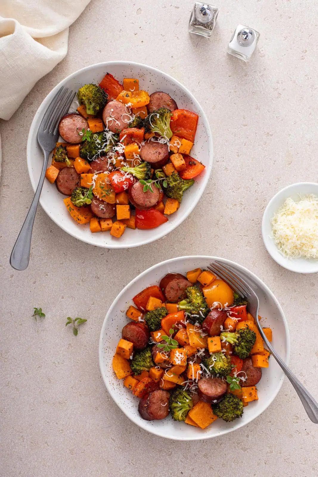 Overhead view of two white bowls, each filled with sheet pan sausage and veggies.