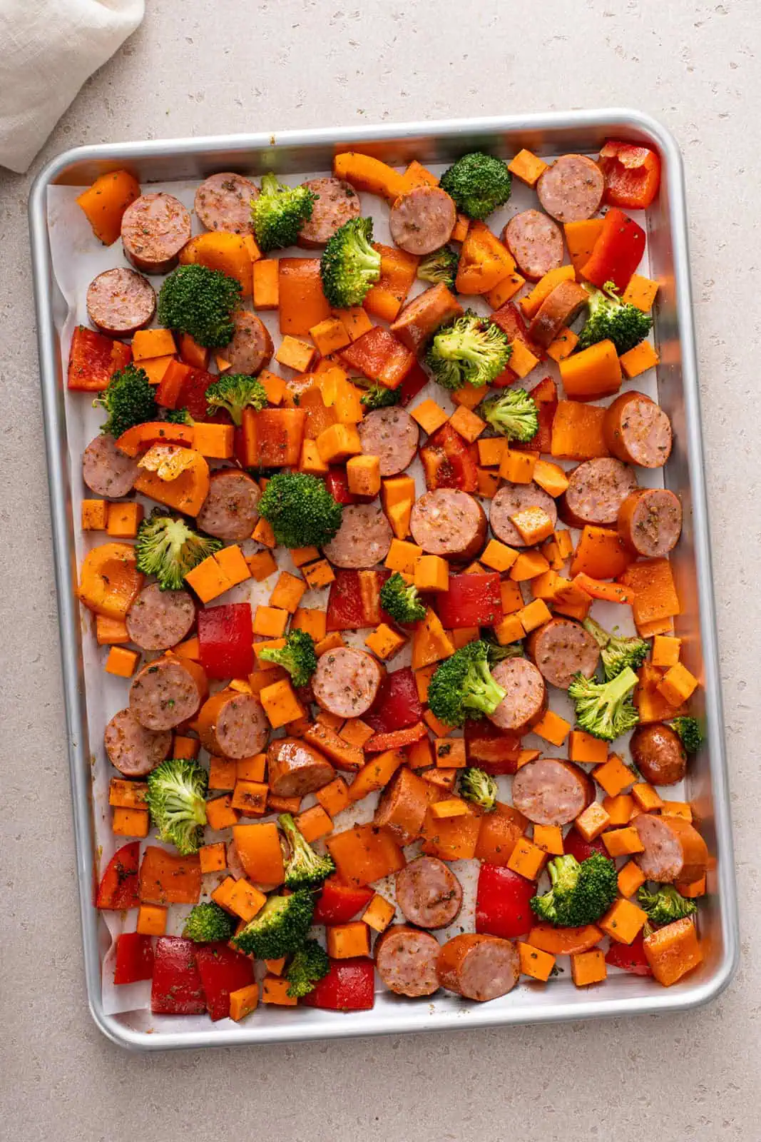 Rimmed sheet pan filled with seasoned sausage and vegetables, ready to go in the oven.