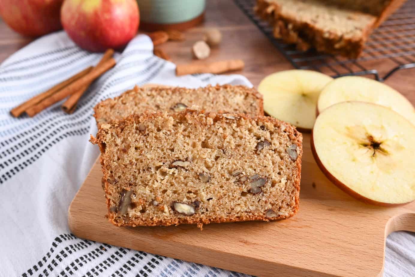 Slices of applesauce bread on a board next to slices of apple.